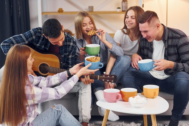 El hombre está tocando la guitarra acústica Un grupo de amigos tienen una fiesta juntos en el interior