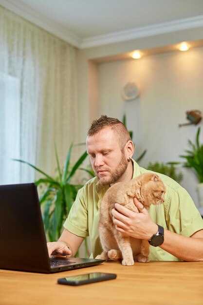 El hombre está trabajando en una computadora portátil negra y el gato está en su mano