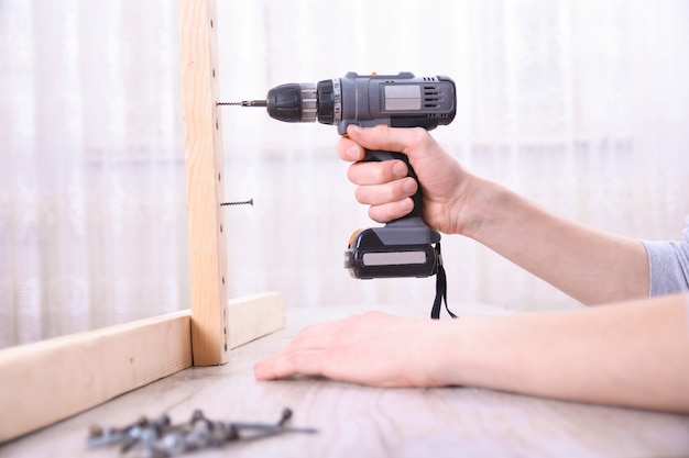 El hombre está trabajando con el ensamblaje de muebles con un destornillador eléctrico en la instalación de una casa nueva: trabajo in situ del técnico utilizando el concepto de herramientas manuales