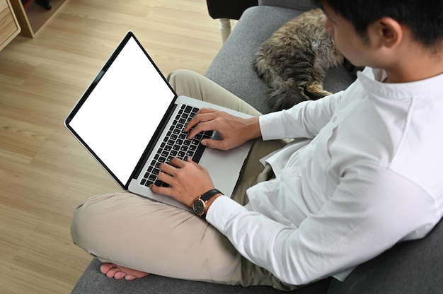 El hombre está usando una computadora portátil con pantalla blanca mientras está sentado en el sofá con su gato