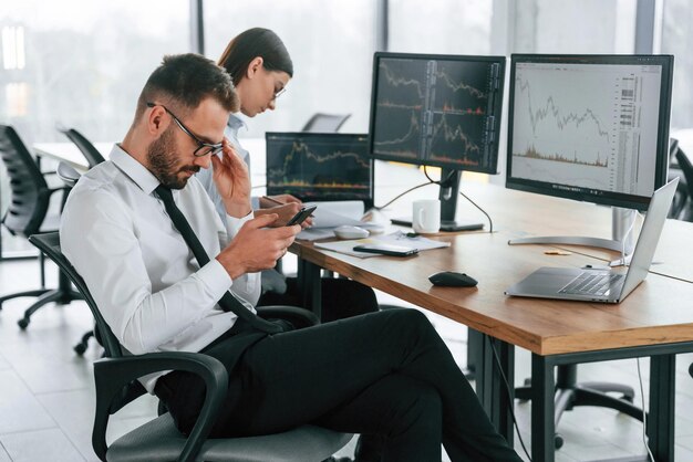El hombre está usando su teléfono inteligente Dos empleados están trabajando juntos en la oficina