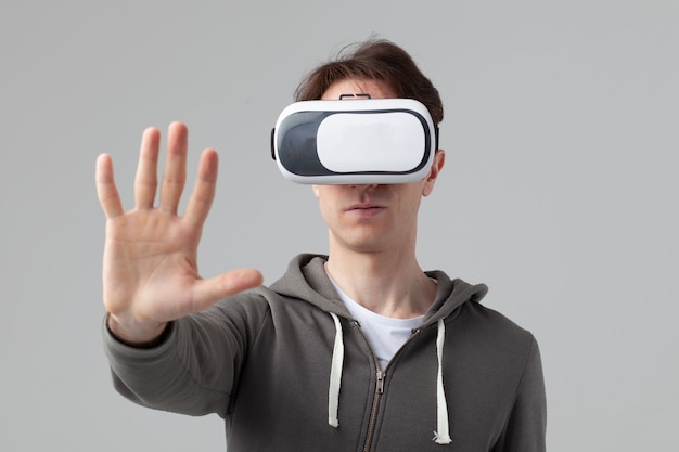 Hombre de estilo casual con gafas VR levanta su brazo aislado sobre fondo gris