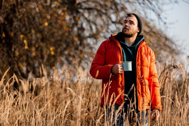 Hombre de estilo en chaqueta con taza de café en otoño rural al aire libre