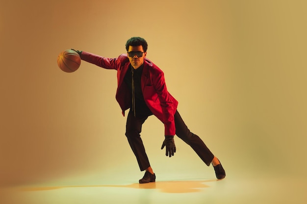 Hombre de estilo highfashion con chaqueta roja jugando baloncesto aislado sobre fondo marrón