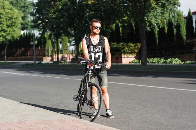 Hombre con estilo joven de pie en la carretera con la bicicleta