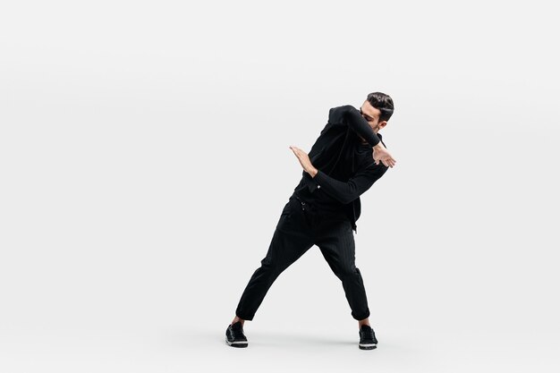 Hombre con estilo de pelo oscuro vestido con una elegante ropa negra está bailando street dance