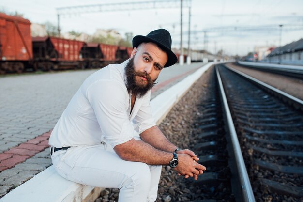 Hombre con estilo sentado cerca de los ferrocarriles