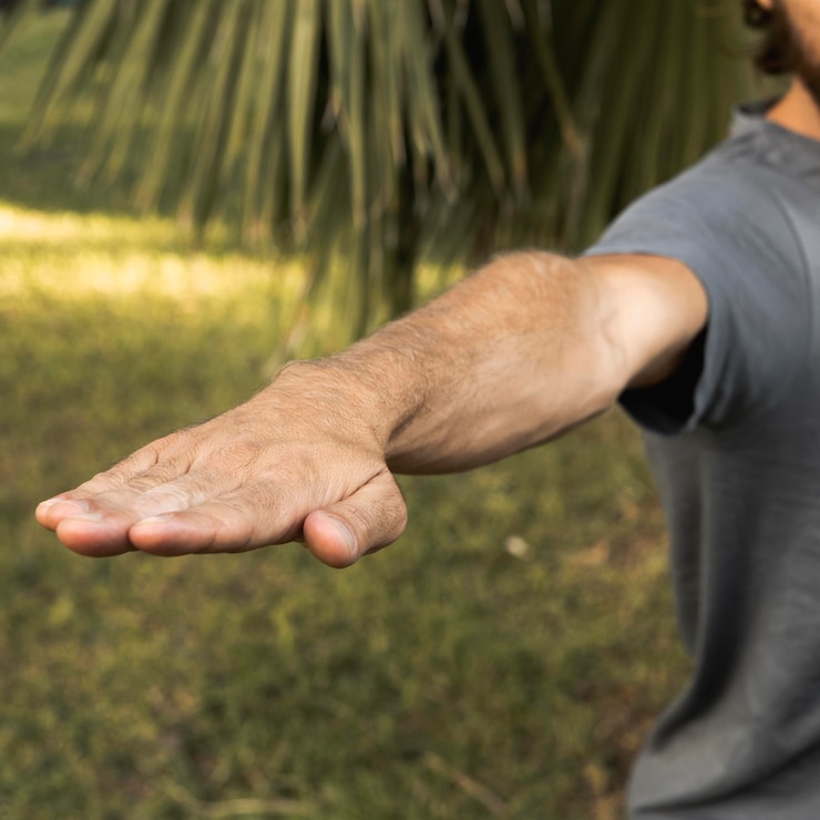 Foto hombre estirando su brazo mientras hace yoga al aire libre