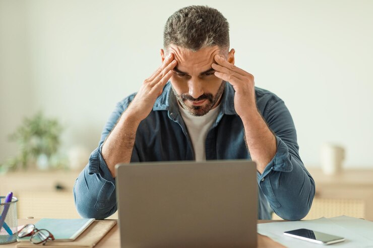 Hombre con estrés y dolor de cabeza mientras mira la computadora portátil en el interior