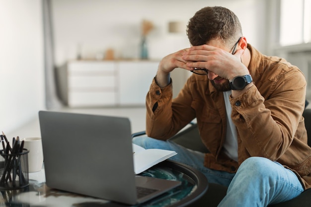 Hombre estresado en la cabeza tocando la computadora portátil que tiene problemas de negocios en el interior