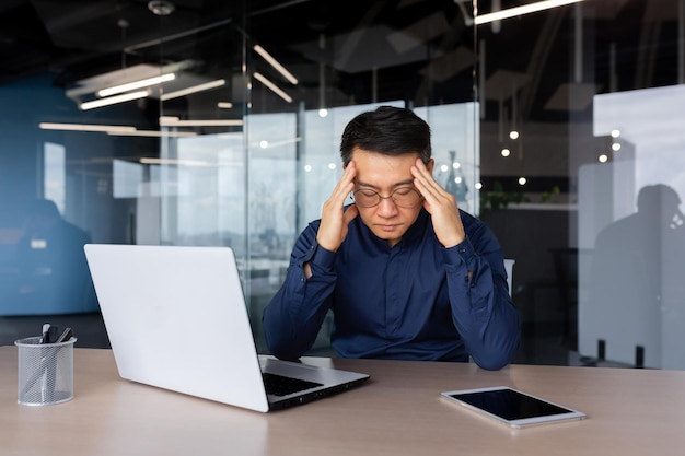 Hombre estresado trabajando dentro de la oficina hombre asiático con exceso de trabajo sentado en el lugar de trabajo triste y deprimido