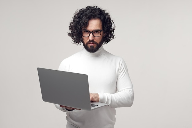 Hombre estricto con gafas escribiendo en una computadora portátil en el estudio