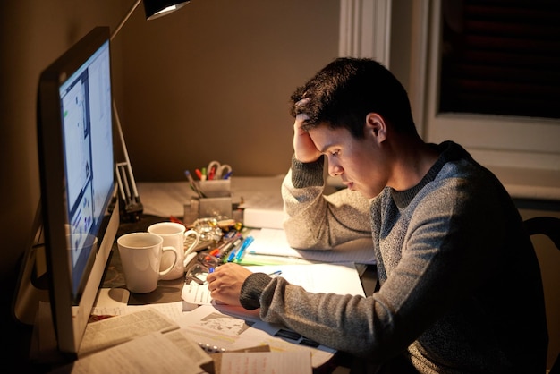 Hombre estudiando y estresado en la noche por computadora para evaluación de exámenes o dolor de cabeza en el dormitorio universitario Educación de estudiantes universitarios masculinos y agotamiento con fatiga por ansiedad y cansado con libros para aprender