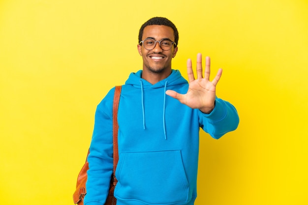 Hombre estudiante afroamericano sobre fondo amarillo aislado contando cinco con los dedos