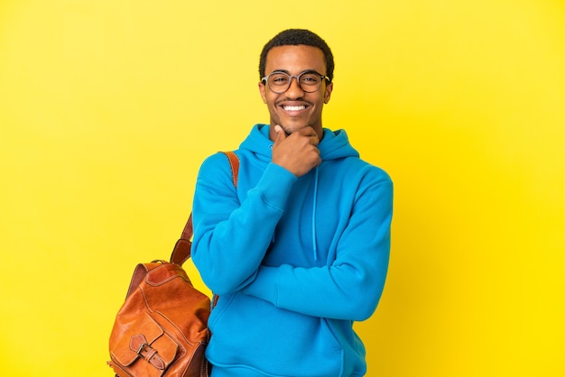 Hombre estudiante afroamericano sobre fondo amarillo aislado con gafas y feliz