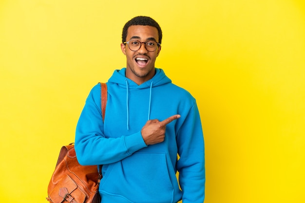Hombre estudiante afroamericano sobre fondo amarillo aislado sorprendido y apuntando hacia el lado
