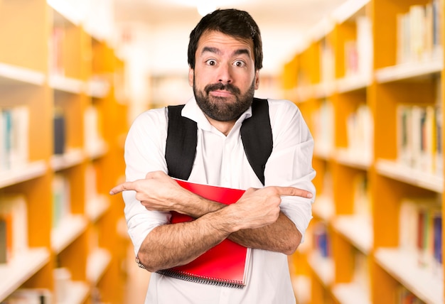 Foto hombre estudiante apuntando a los laterales con dudas en la biblioteca defocused