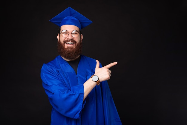 Hombre estudiante barbudo sorprendido en soltero azul apuntando en dirección opuesta