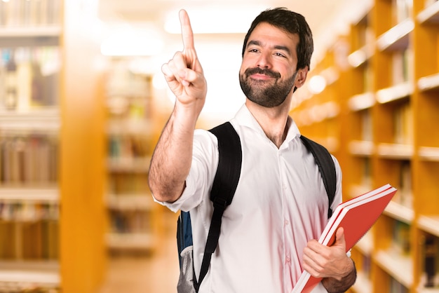 Hombre estudiante tocando en pantalla transparente en la biblioteca defocused