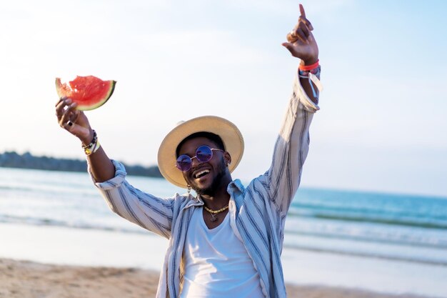 El hombre de etnia negra disfruta de las vacaciones de verano en la playa comiendo una sandía divirtiéndose