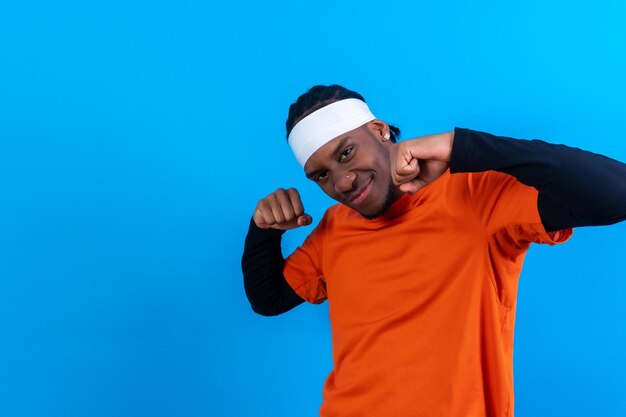 Hombre de etnia negra con ropa naranja de fondo azul sonriendo y pasándoselo bien bailando