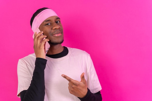 Hombre de etnia negra con un teléfono vestido de rosa sobre un fondo rosa apuntando al teléfono