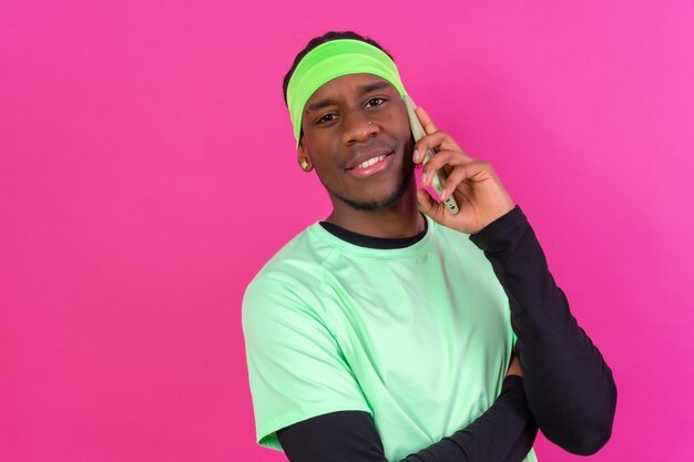 Hombre de etnia negra con un teléfono vestido de verde con un fondo rosa sonriendo hablando por teléfono