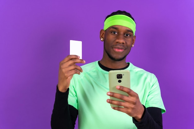 Hombre de etnia negra con un teléfono vestido de verde con una tarjeta de crédito de concepto de venta en línea de fondo rosa