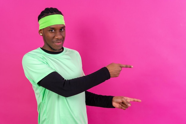 Hombre de etnia negra vestido de verde con un fondo rosa apuntando a un espacio libre de copia derecha