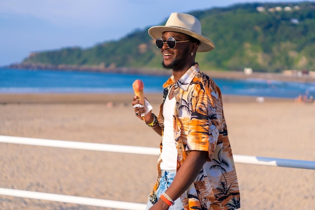 El hombre étnico negro disfruta de las vacaciones de verano en la playa comiendo helado