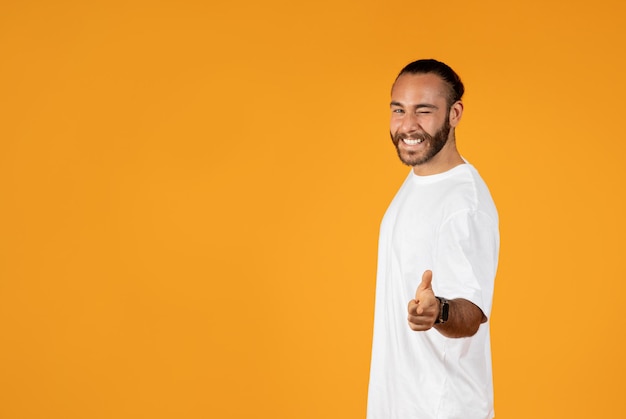 Un hombre europeo adulto alegre y confiado con una camiseta blanca guiña un ojo y muestra el dedo a la cámara