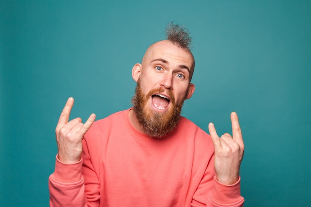 Hombre europeo barbudo en melocotón casual aislado, gritando con expresión loca haciendo símbolo de rock con las manos arriba
