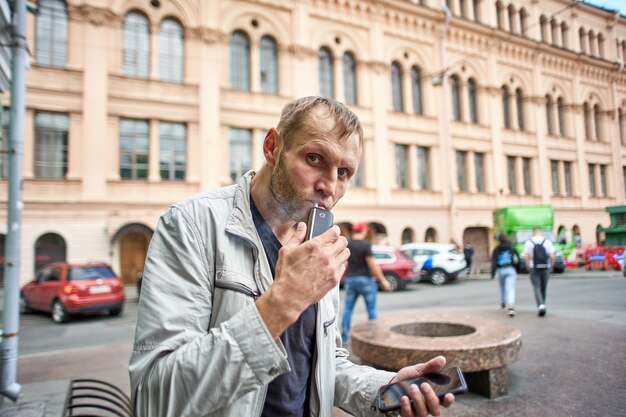 Hombre europeo fuma cigarrillos electrónicos en la concurrida calle