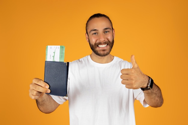 Un hombre europeo milenario satisfecho con camiseta blanca muestra pasaporte y boletos disfruta del estilo de vida