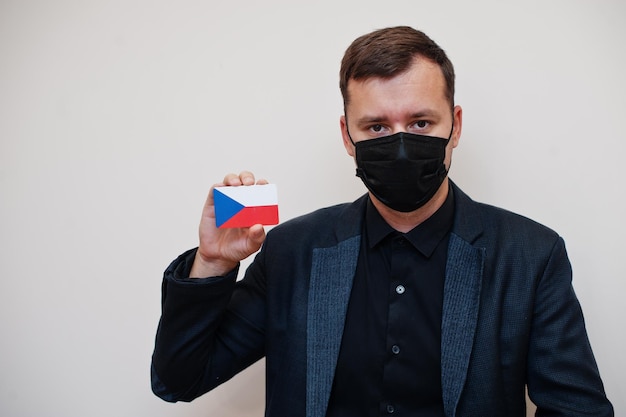 El hombre europeo usa negro formal y protege la máscara facial sostiene la tarjeta de la bandera de la República Checa aislada sobre fondo blanco Europa coronavirus Covid concepto de país