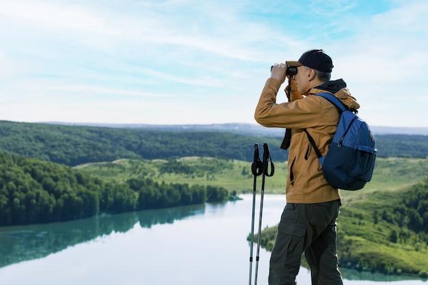 Hombre excursionista mirando con binoculares en la montaña. Senderismo estilo de vida de personas activas.