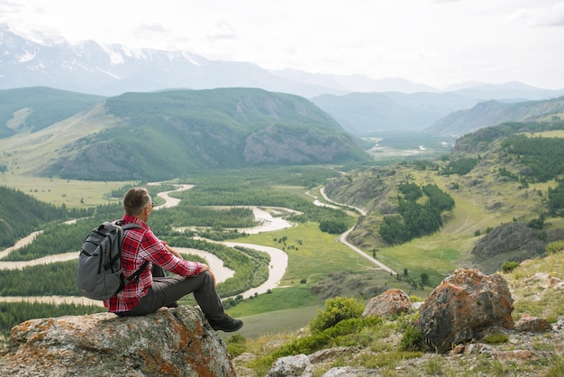 Hombre excursionista sentado en la cima de la montaña mirando el hermoso paisaje panorámico El concepto de viajes turísticos y soledad masculina