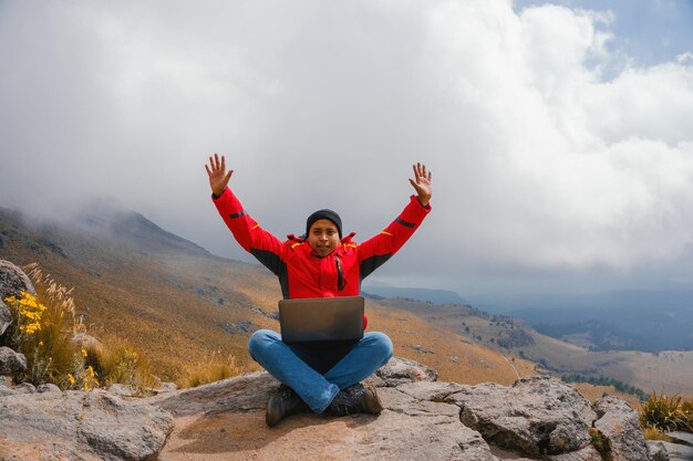 Hombre de éxito joven que usa la computadora portátil y los brazos abiertos en el pico de la montaña celebran su libertad