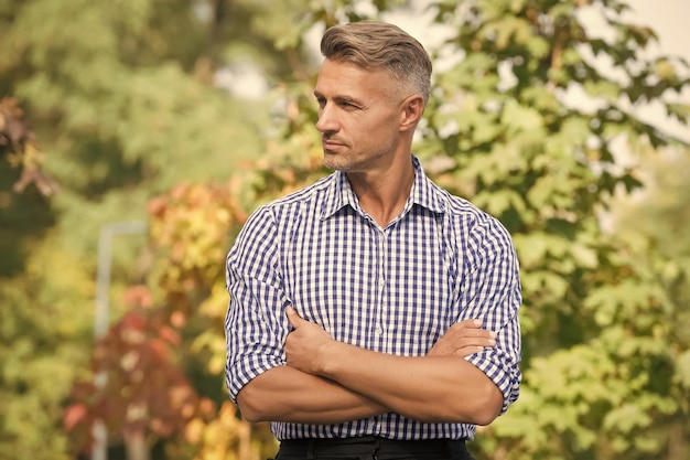 Un hombre exitoso y carismático, un hombre guapo, ha arreglado el cabello canoso, un hombre maduro, cruzó las manos al aire libre, otoño o primavera, moda casual, moda masculina y belleza, un día normal y corriente.