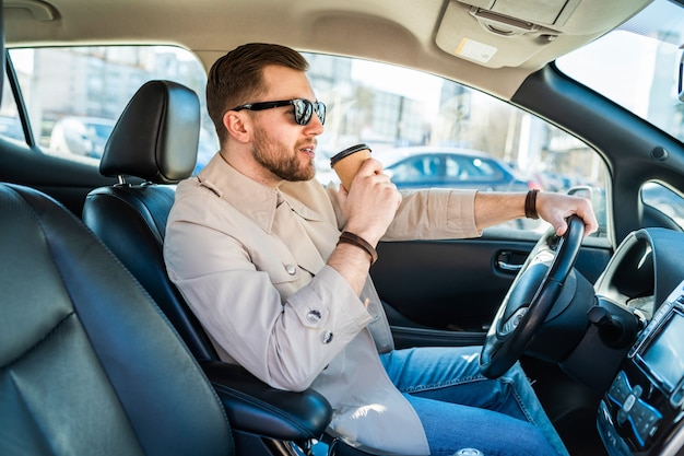 Hombre exitoso conduciendo un coche con una taza de café en la mano