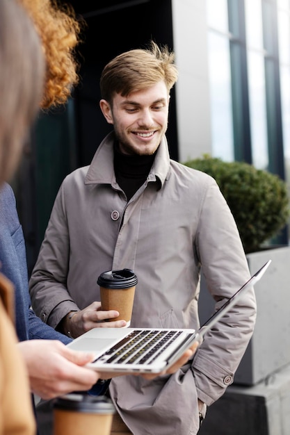 Hombre exitoso de pie al aire libre hablando con su compañero de trabajo mirando la computadora portátil Educación en línea de trabajo en línea