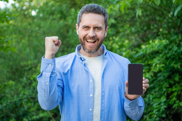 Hombre exitoso que presenta un teléfono inteligente hombre que presenta un teléfono inteligente hombre al aire libre que presenta la pantalla del teléfono inteligente con una foto de espacio de copia del hombre que presenta un teléfono inteligente