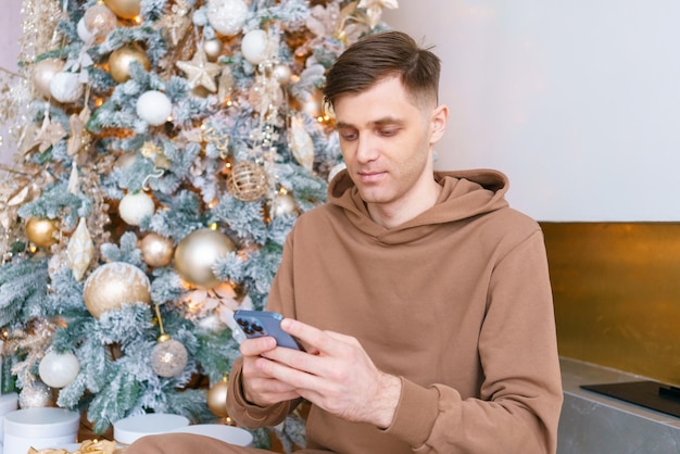 Hombre exitoso que usa un teléfono inteligente contra un árbol de Navidad Público de las redes sociales