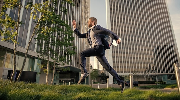 Hombre exitoso en ropa formal corriendo con la computadora fuera de la oficina, date prisa