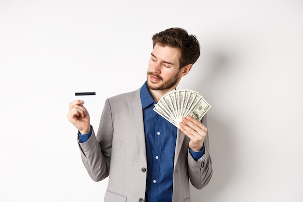 Foto hombre exitoso sosteniendo billetes de un dólar y mirando tarjeta de crédito de plástico