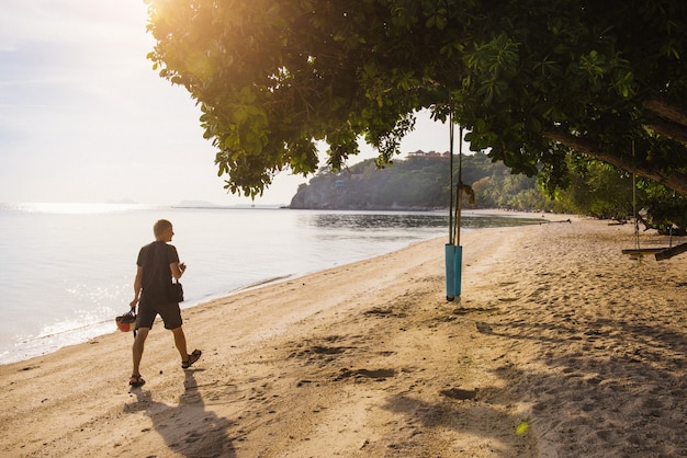 Foto hombre explorando la playa para descansar después del trabajo cerca del mar. sol a través de las hojas del árbol y el columpio.