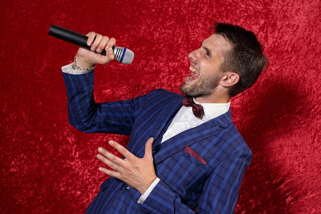 Hombre expresivo en traje cantando canciones en el micrófono mientras actúa sobre fondo rojo en el estudio