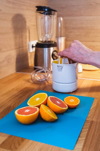 El hombre exprime jugo en un exprimidor de naranjas rojas y naranjas picadas en la cocina