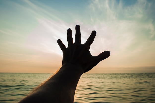 Un hombre extiende su mano hacia el mar al atardecer o al amanecer.