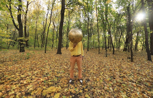 hombre con una extraña cabeza de bola dorada en el bosque